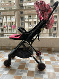 Black and pink stroller on a tiled floor with buildings in the background