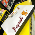 White board with 'Reyansh' written on it, placed on a yellow surface with cartoon characters.