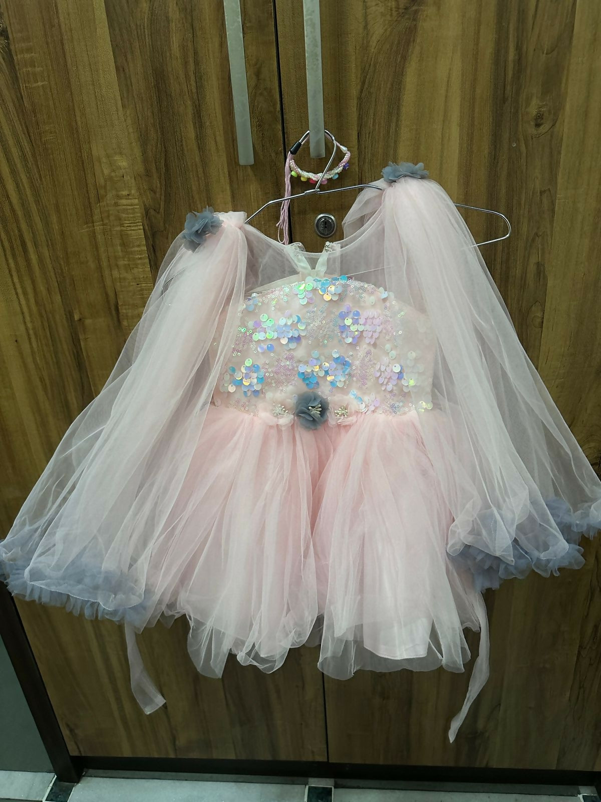 Children's dress with sequin embellishments and tulle skirt on a hanger against a wooden background