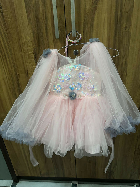 Children's dress with sequin embellishments and tulle skirt on a hanger against a wooden background