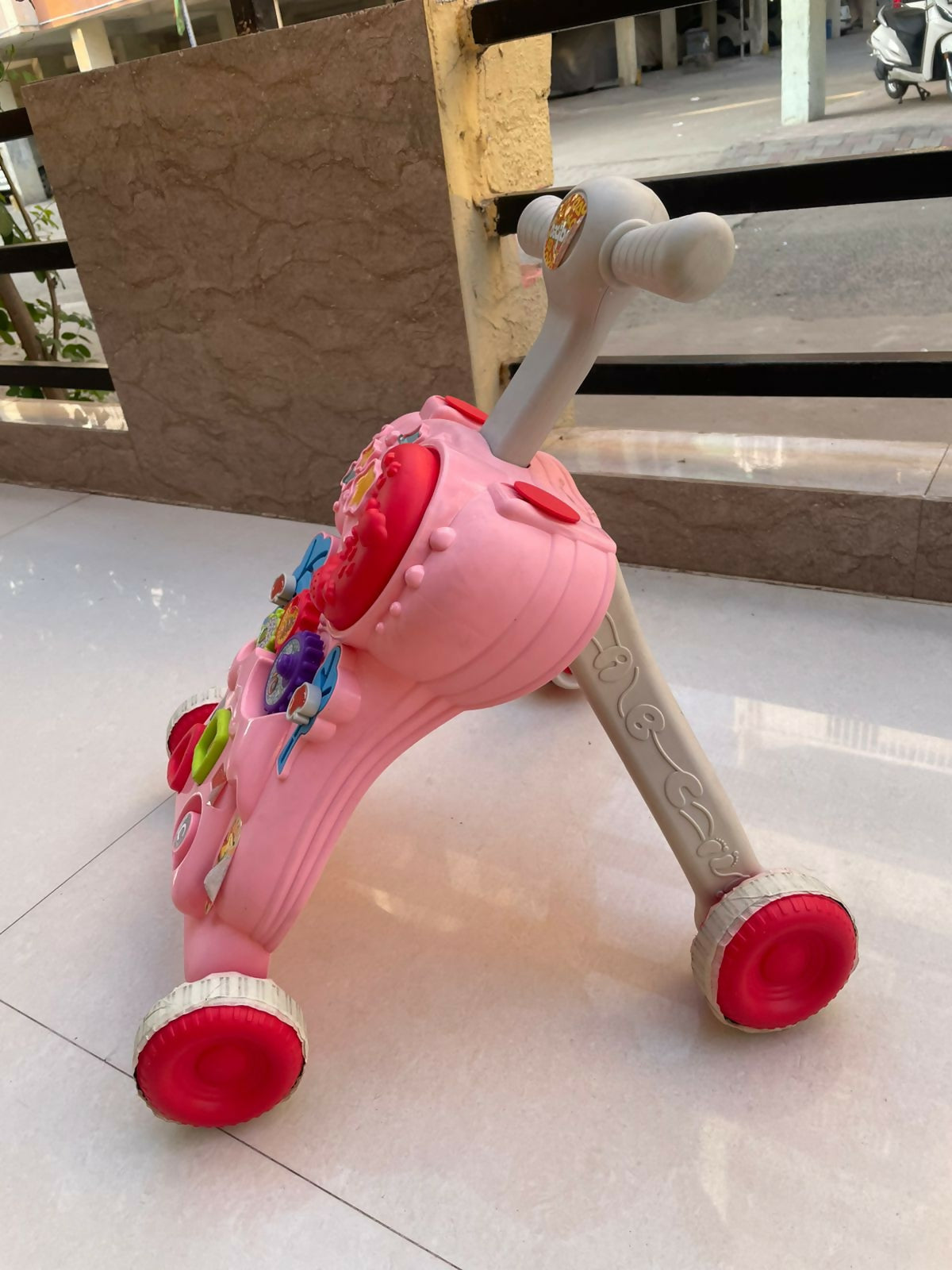 Pink children's scooter with colorful decorations on a tiled floor.