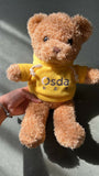 Teddy bear wearing a yellow shirt with 'Osda' printed on it, held by a person.