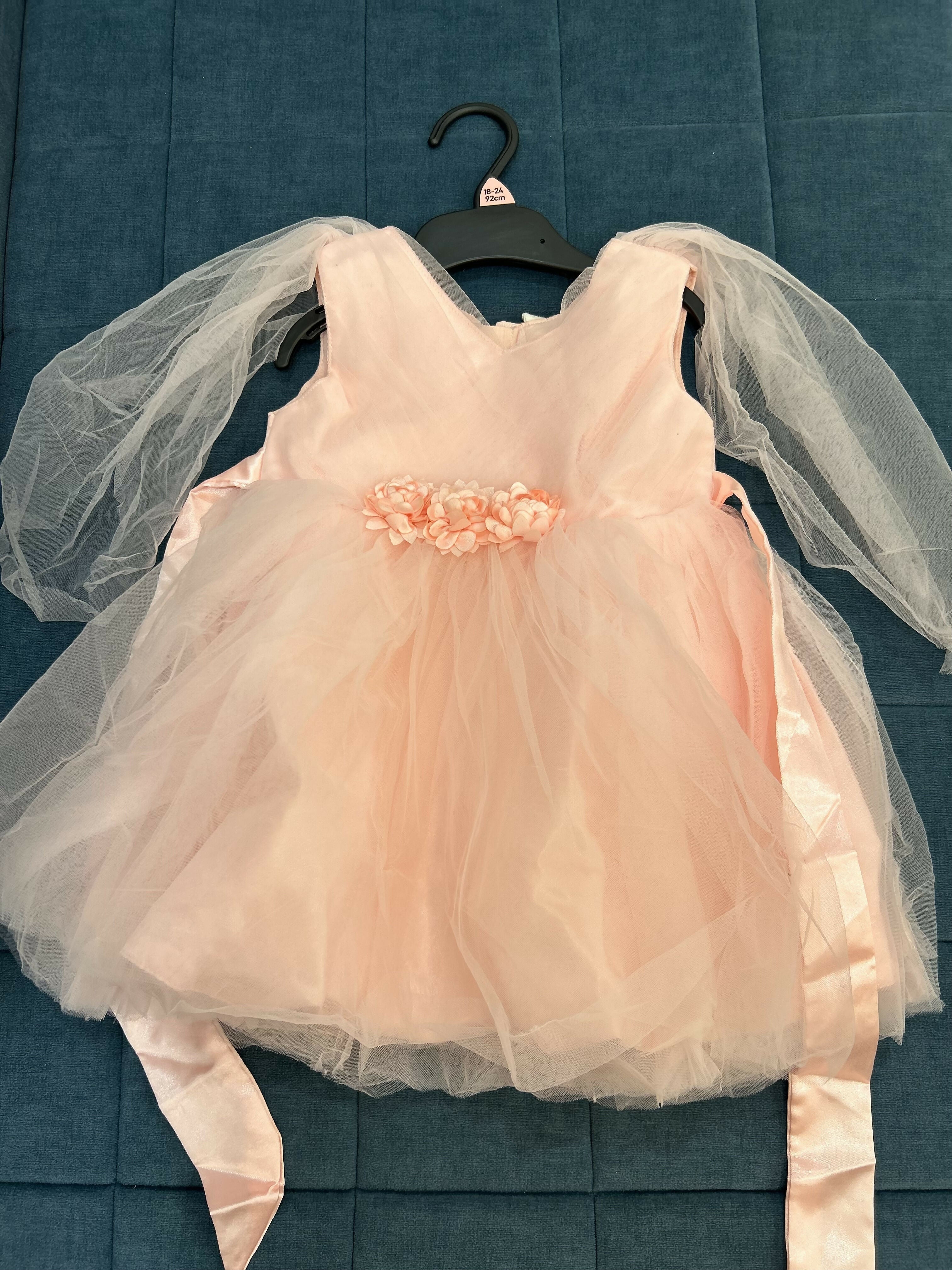 Pink dress with sheer sleeves on a hanger against a blue textured background