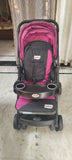Pink and black stroller on a tiled floor with curtains in the background