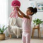 Child holding a pink knitted octopus toy in a room with a couch and plants.