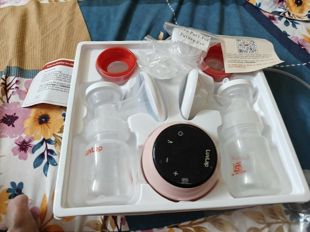 Breast pump set with bottles and control panel in a box on a floral-patterned surface.