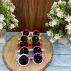 Set of colorful children's sunglasses on a wooden board with flowers on either side.