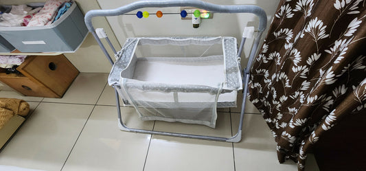 Baby bassinet on a tiled floor with a blanket and storage bins in the background