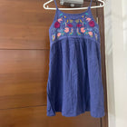 Blue dress with floral embroidery on a hanger against a wooden door.