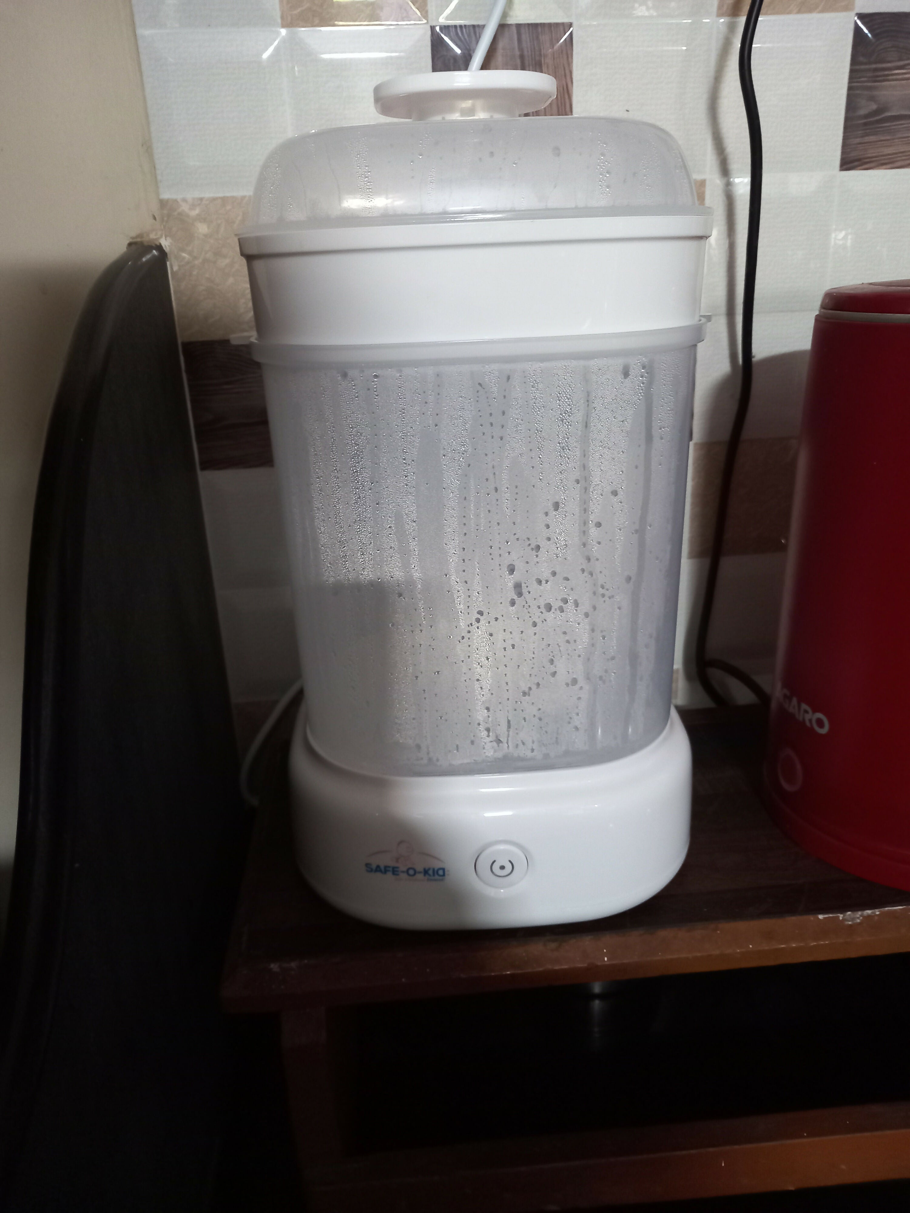 White electronic device on a wooden surface with a red container in the background.