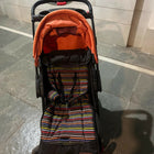 Baby stroller with orange cover and striped seat on a stone floor.