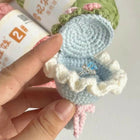 Hand holding a small crocheted ring box with a ring inside, against a blurred background.