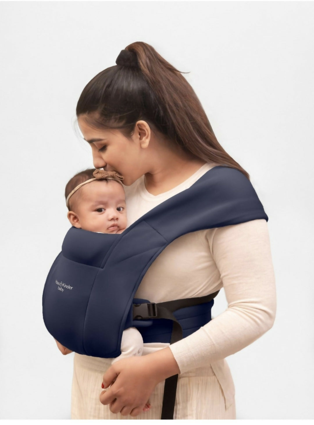 Woman holding a baby in a navy blue baby carrier against a white background