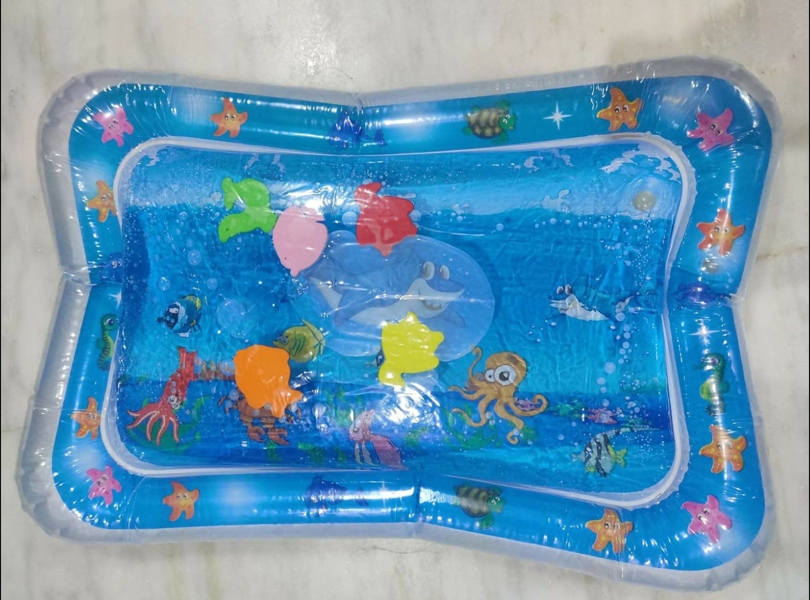Children's inflatable pool with ocean-themed toys on a light gray background