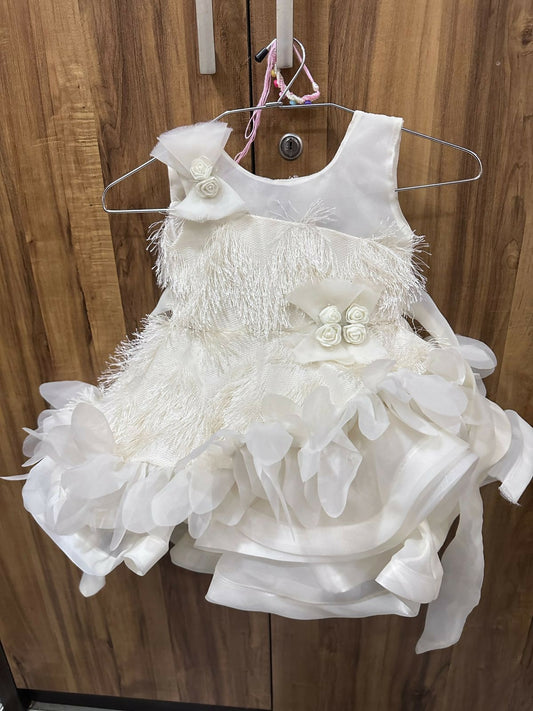 White children's dress with floral details on a hanger against a wooden background