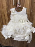 White children's dress with floral details on a hanger against a wooden background