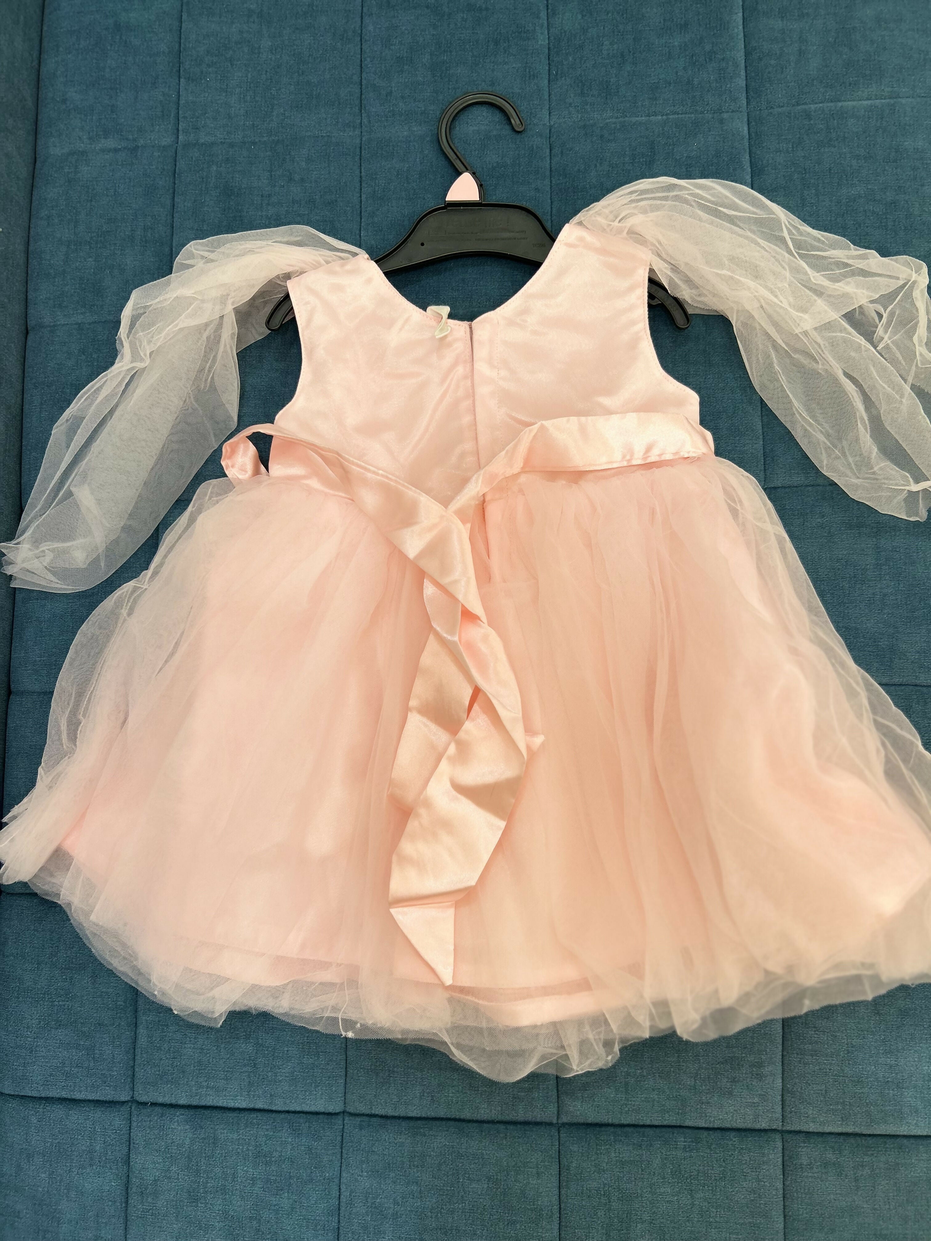 Pink dress with sheer sleeves on a hanger against a blue textured background