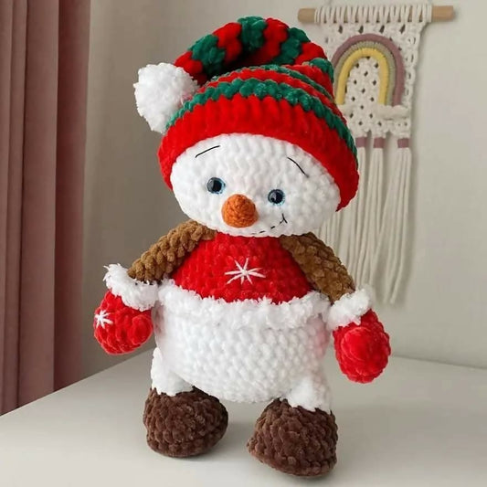 Crocheted snowman toy with a red hat and scarf on a white surface.