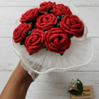 Bouquet of red knitted roses on a white stand with a wooden tag below.