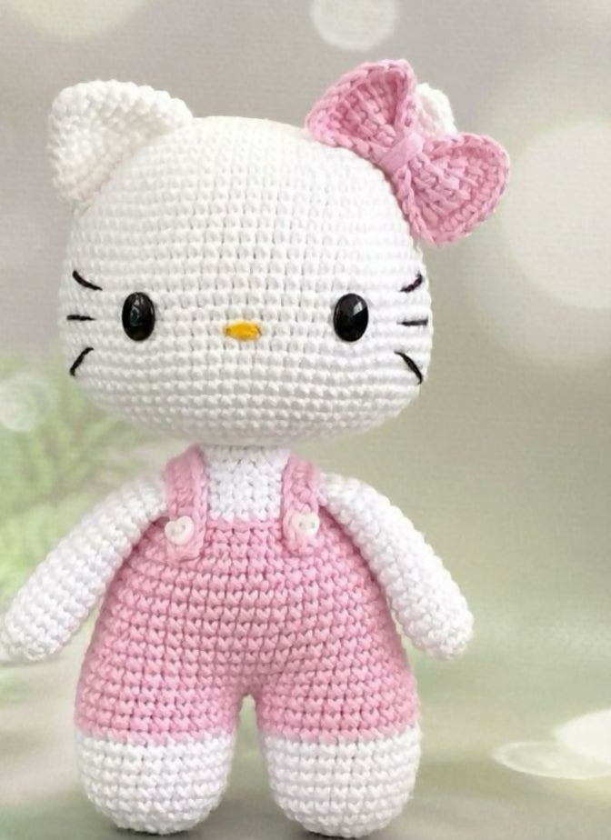 Crocheted toy resembling a character with a pink bow and pink overalls on a light background