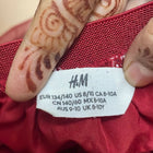 Red garment with an H&M label and hand with henna designs.