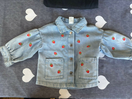 Denim jacket with strawberry patterns on a gray surface with heart shapes.