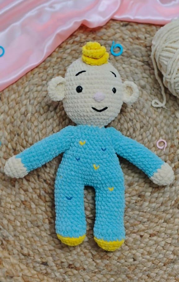 Crocheted toy with blue outfit and yellow accents on a textured surface