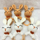 Set of crocheted bunny rattle toys with wooden rings on a soft surface.