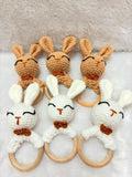 Set of crocheted bunny rattle toys with wooden rings on a soft surface.