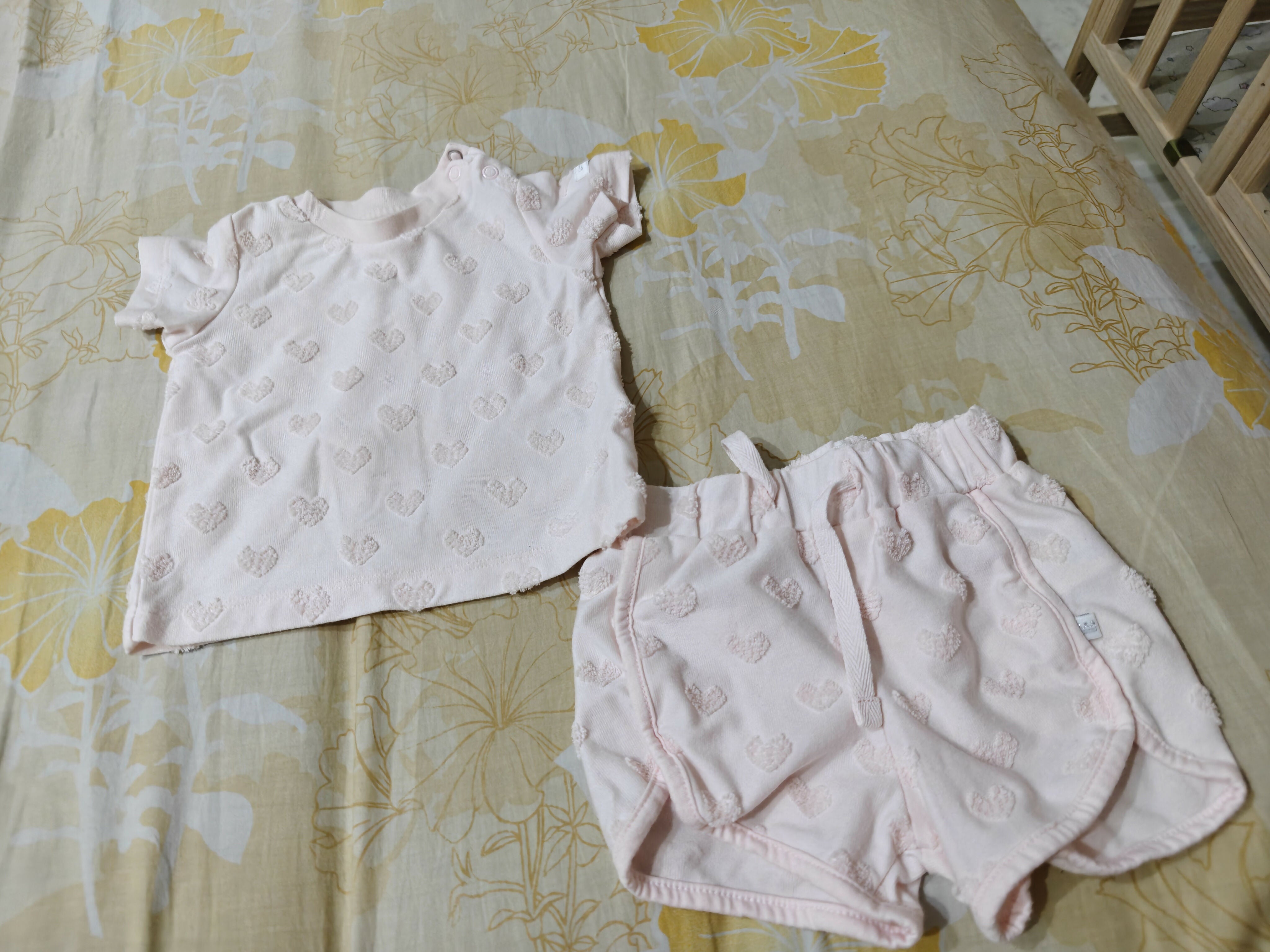 White baby top and pink baby shorts on a floral-patterned bedspread