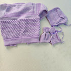Purple knitted baby outfit with a hat on a light gray background