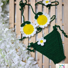 Crocheted daisy flowers and green leaves with white flowers.