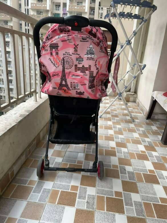 Pink stroller cover with Eiffel Tower design on a tiled balcony floor.
