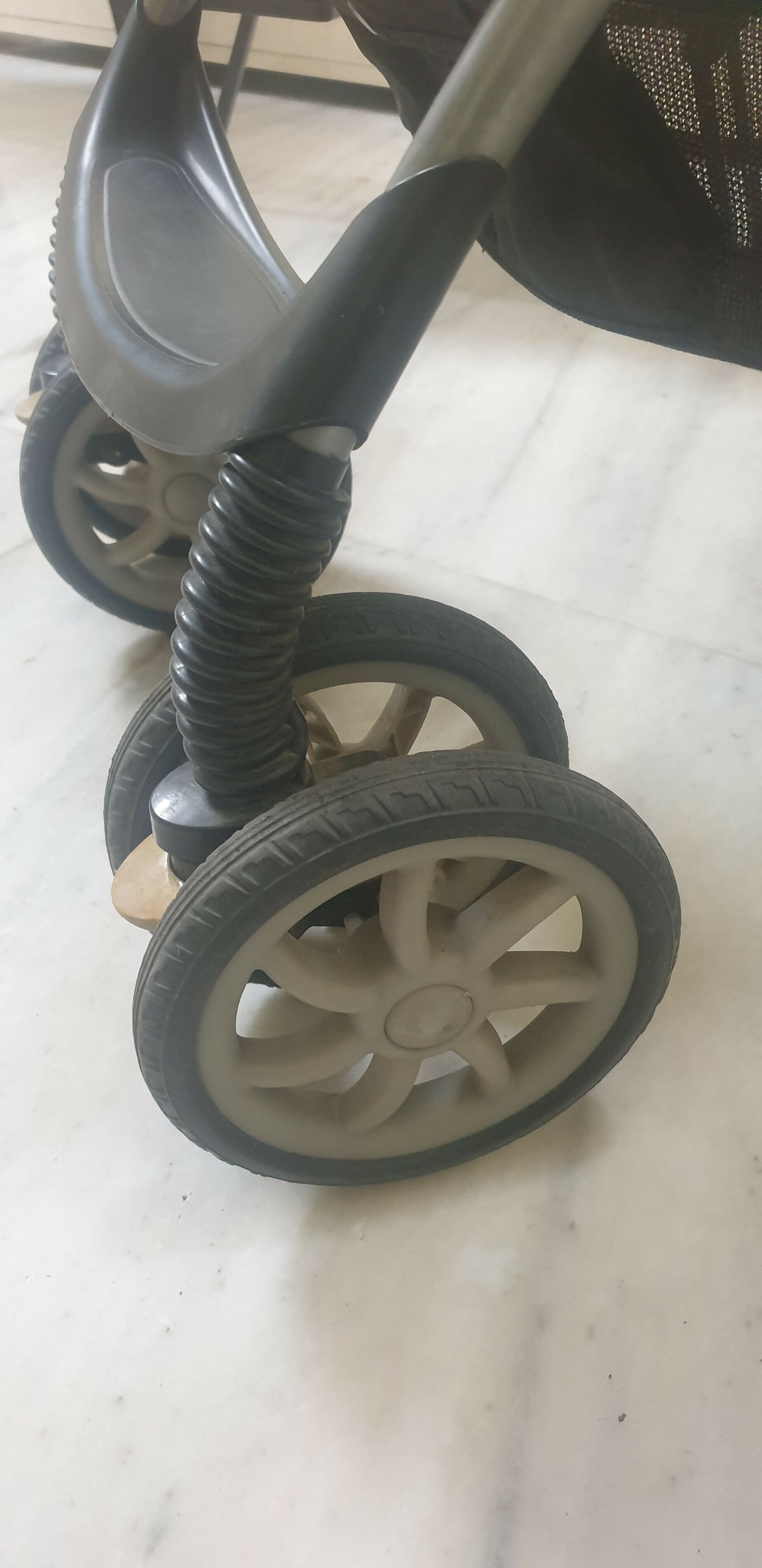 Close-up of a stroller wheel with a spring mechanism on a light-colored floor.