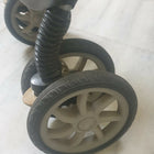 Close-up of a stroller wheel with a spring mechanism on a light-colored floor.