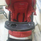 Red and black stroller with floral pattern on a white floor.