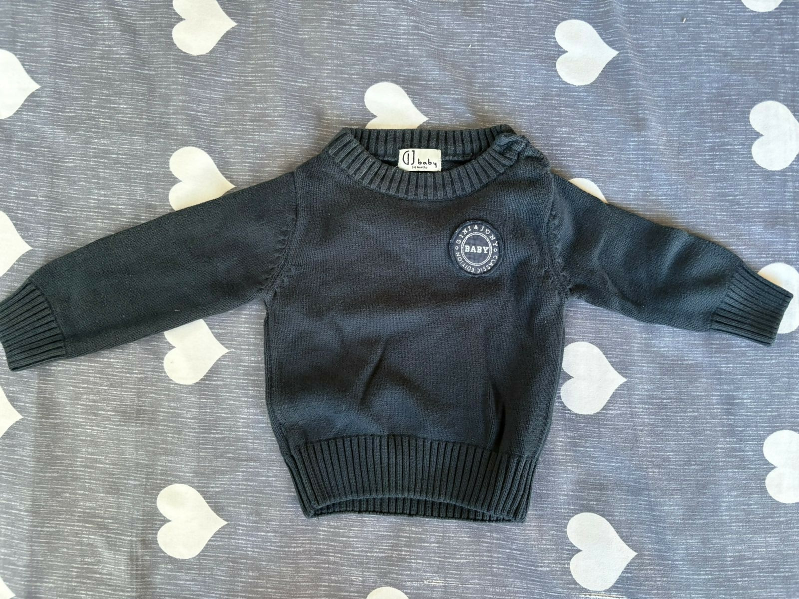 Black sweater with a logo on a gray surface with heart patterns