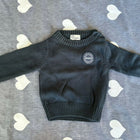 Black sweater with a logo on a gray surface with heart patterns