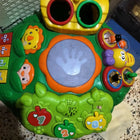 Colorful baby activity table with interactive buttons, music features, shape sorter holes, and small toy elements, designed for early learning and play.