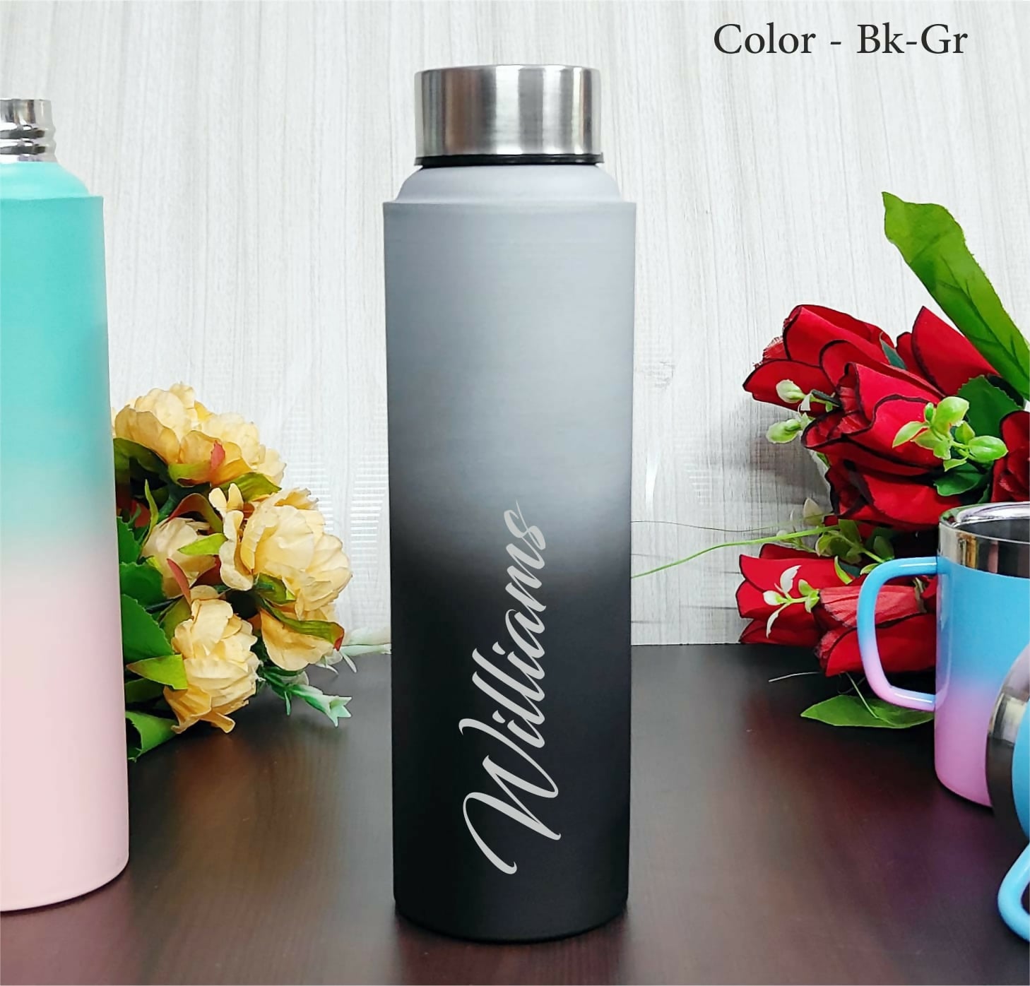Gradient water bottle with 'Williams' engraving on a wooden surface with flowers in the background.