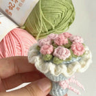 Handmade crochet flower arrangement with pink and green yarn on a white background