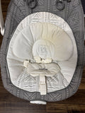 Baby bouncer with gray and white patterned cover on a wooden floor