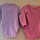 Two baby bodysuits, one purple and one pink, with white polka dots