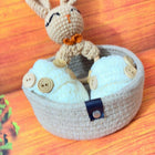 Small crochet rabbit toy sitting inside a round basket on a wooden surface