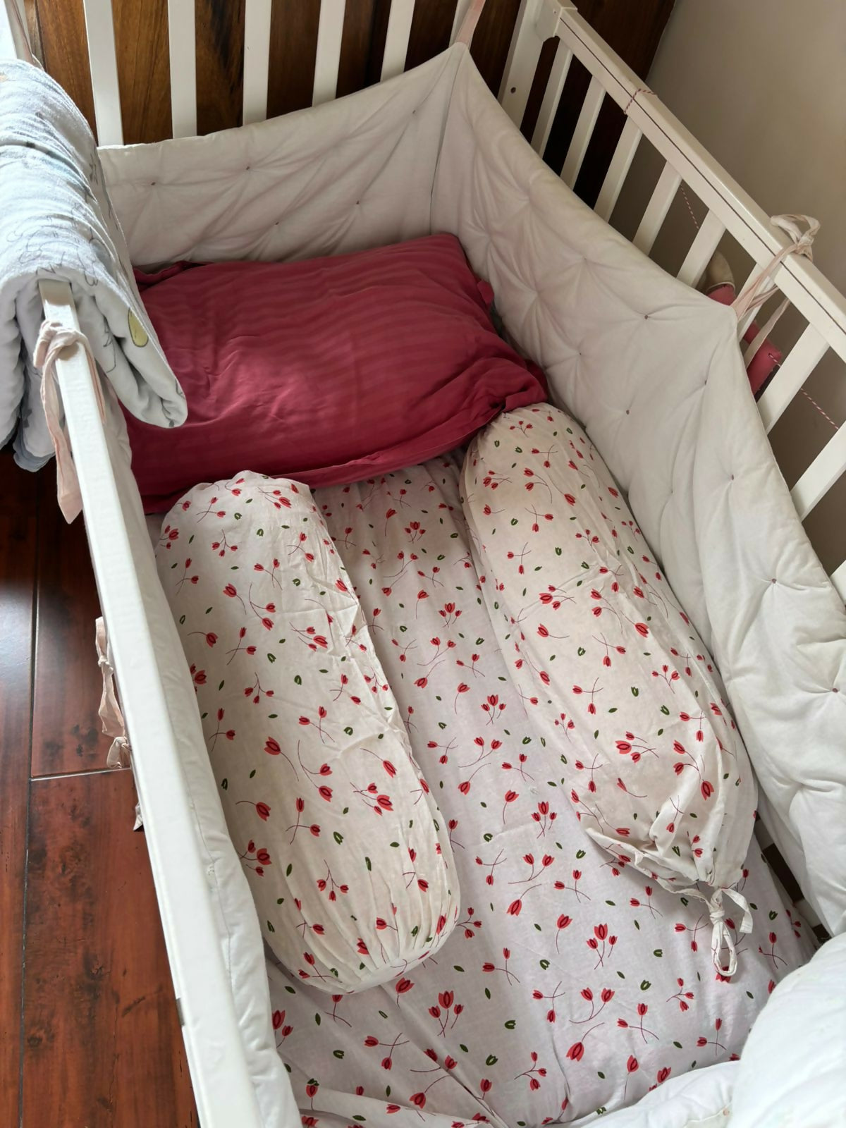 Crib with red and white bedding and pillows on a wooden floor.