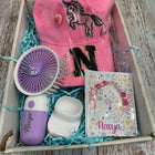 Box containing a pink cap with a horse design, a purple and white toy, a small white container, and a book with a pony design on a wooden surface.