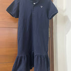 Navy blue dress with a brand logo on a hanger against a wooden door.