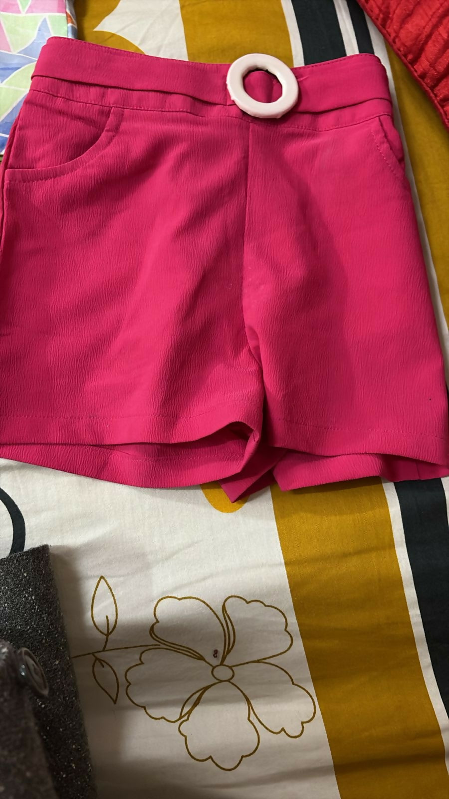 Pink shorts with a wooden ring on a patterned fabric background