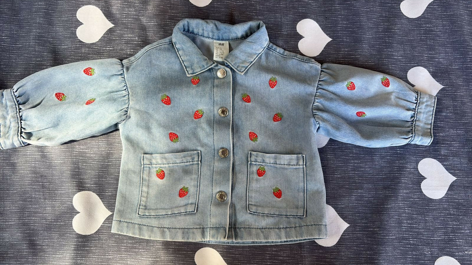 Children's denim outfit with strawberry patterns on a gray background with heart shapes.