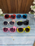 Set of colorful children's sunglasses with decorative bows on a wooden surface.